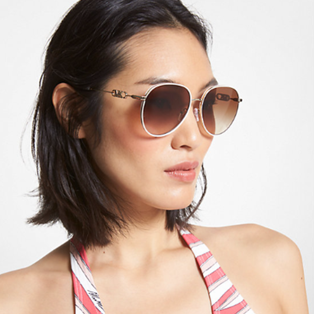 Femme portant des lunettes de soleil Michael Kors avec une monture dorée et des verres teintés marron