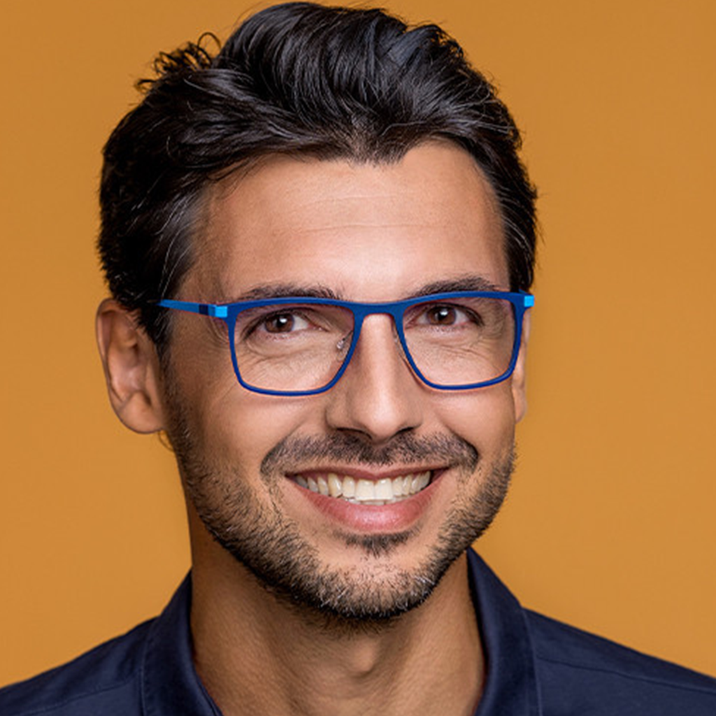 Homme souriant portant des lunettes bleues avec une chemise foncée sur un fond orange