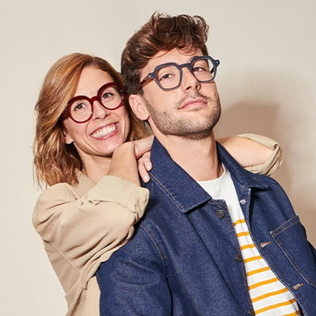 Couple souriant portant des lunettes de créateur, la femme en rouge et l'homme en bleu