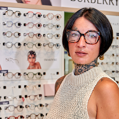 Femme essayant des lunettes devant un présentoir de montures chez Luneo Opticiens