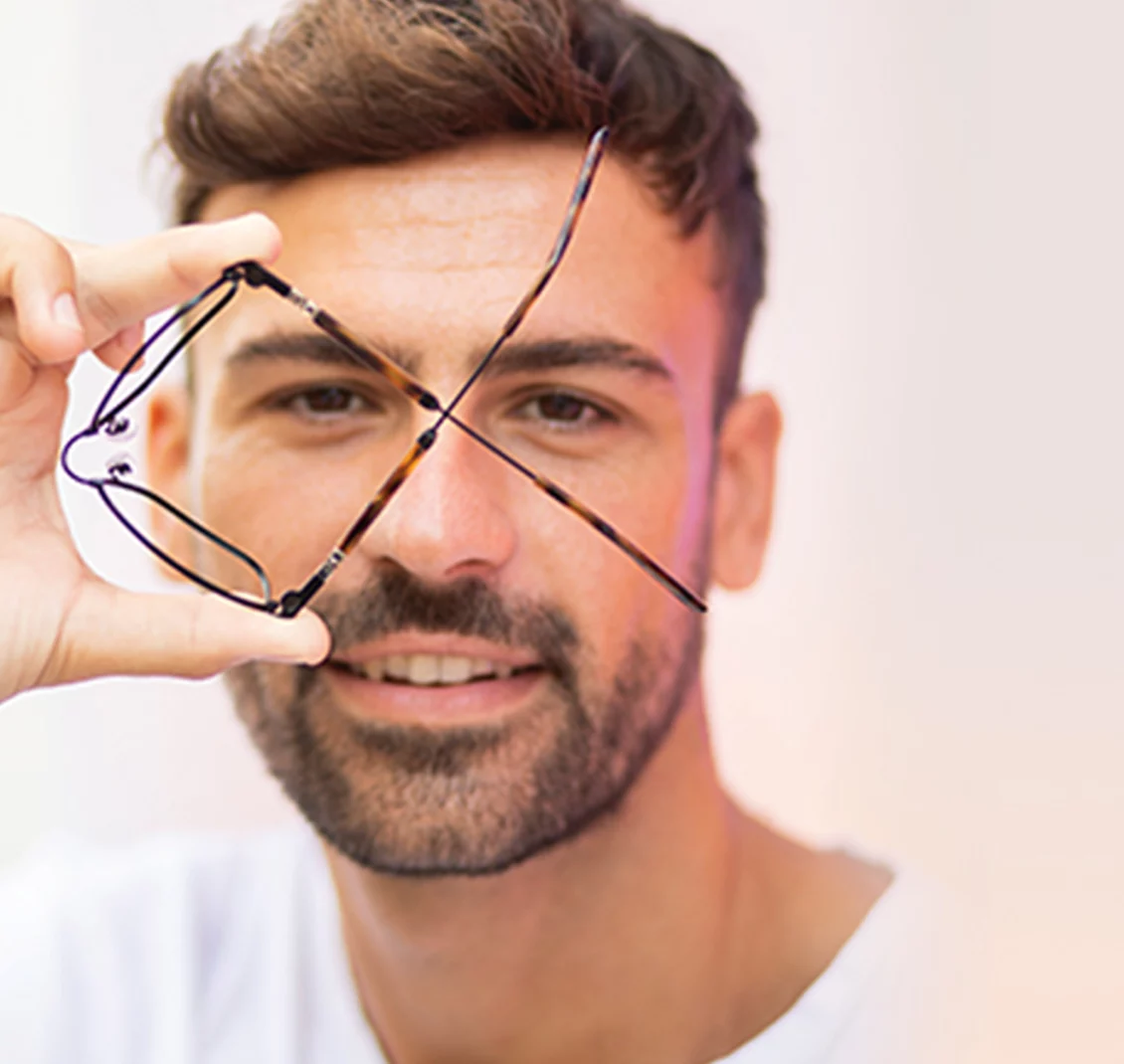 Homme souriant tenant des lunettes devant son visage chez Luneo Opticiens