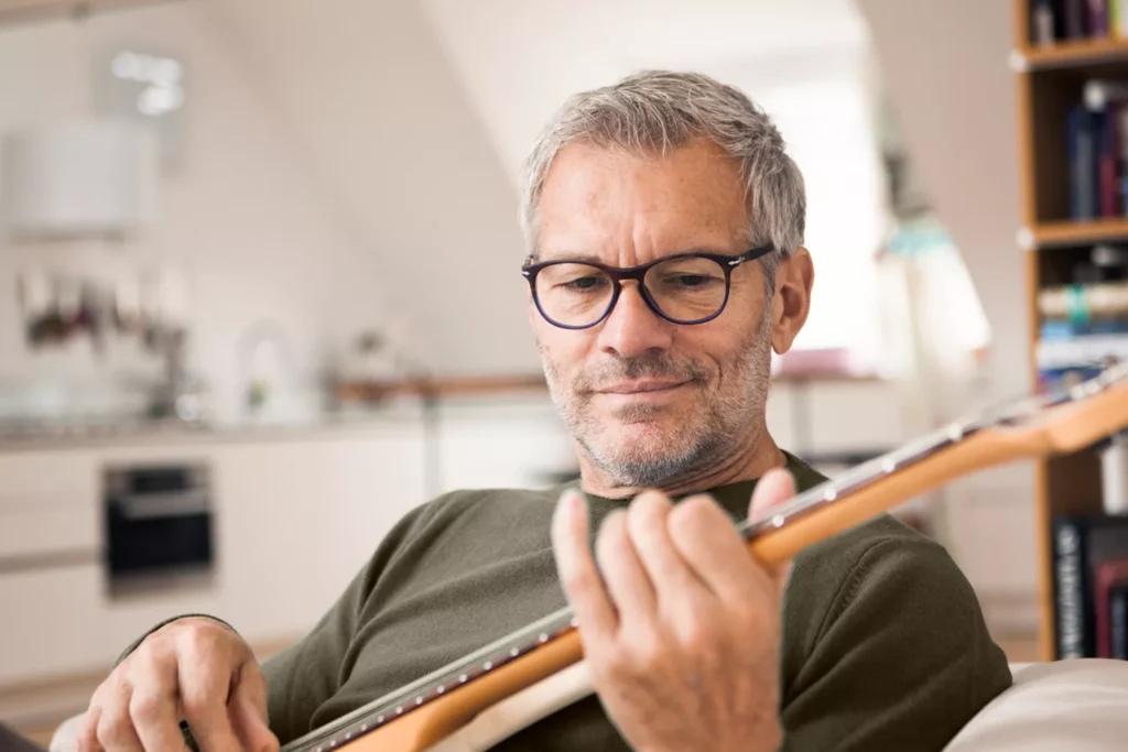 Homme mature avec des lunettes jouant de la guitare dans un salon chez Luneo Opticiens